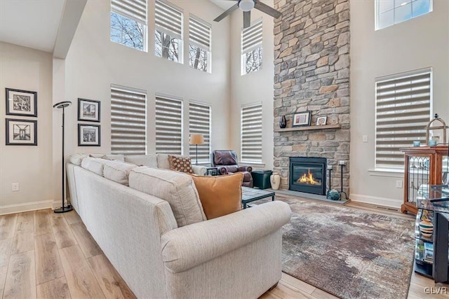 living room with ceiling fan, a towering ceiling, a fireplace, and light hardwood / wood-style floors