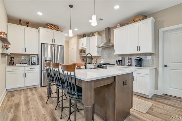 kitchen with white cabinetry, appliances with stainless steel finishes, decorative light fixtures, and wall chimney range hood