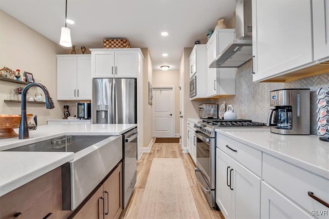 kitchen featuring white cabinetry, appliances with stainless steel finishes, decorative light fixtures, and wall chimney exhaust hood