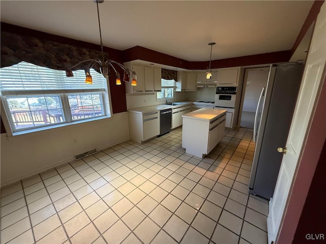 kitchen featuring sink, stainless steel fridge, white oven, a center island, and white cabinets