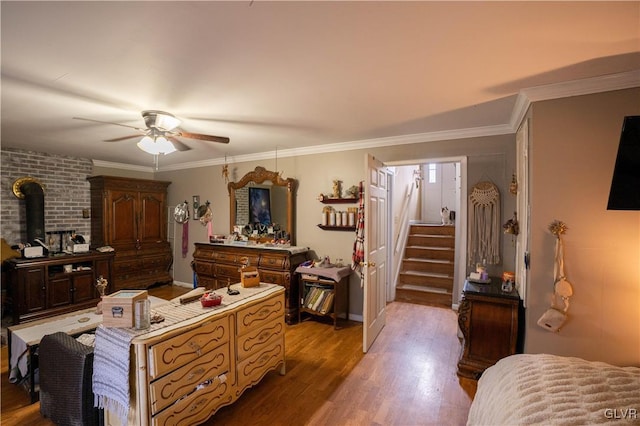 bedroom with ornamental molding, a wood stove, ceiling fan, and light wood-type flooring