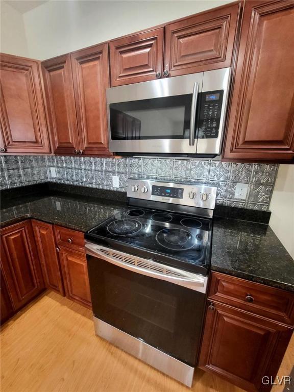 kitchen featuring stainless steel appliances, tasteful backsplash, light hardwood / wood-style flooring, and dark stone counters