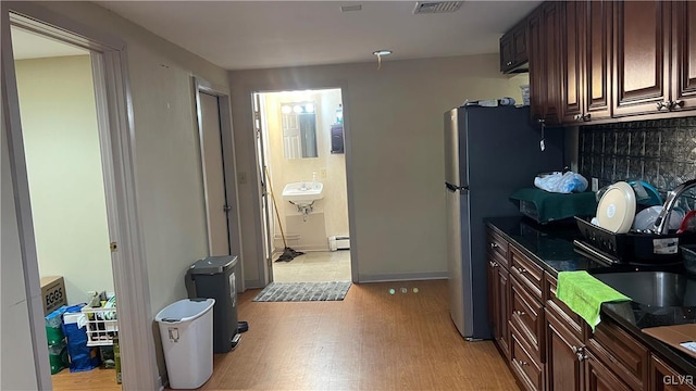 kitchen with sink, light hardwood / wood-style flooring, stainless steel refrigerator, baseboard heating, and dark brown cabinetry