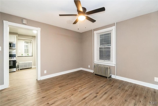 unfurnished room with hardwood / wood-style flooring, ceiling fan, and radiator heating unit