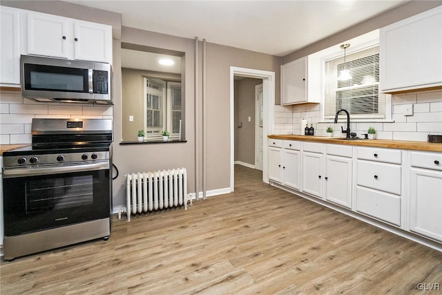 kitchen with butcher block counters, white cabinetry, radiator heating unit, stainless steel appliances, and light hardwood / wood-style floors