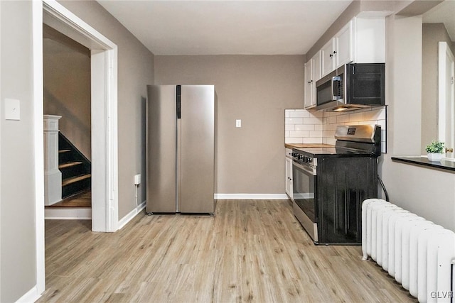 kitchen with white cabinetry, light wood-type flooring, appliances with stainless steel finishes, radiator heating unit, and backsplash