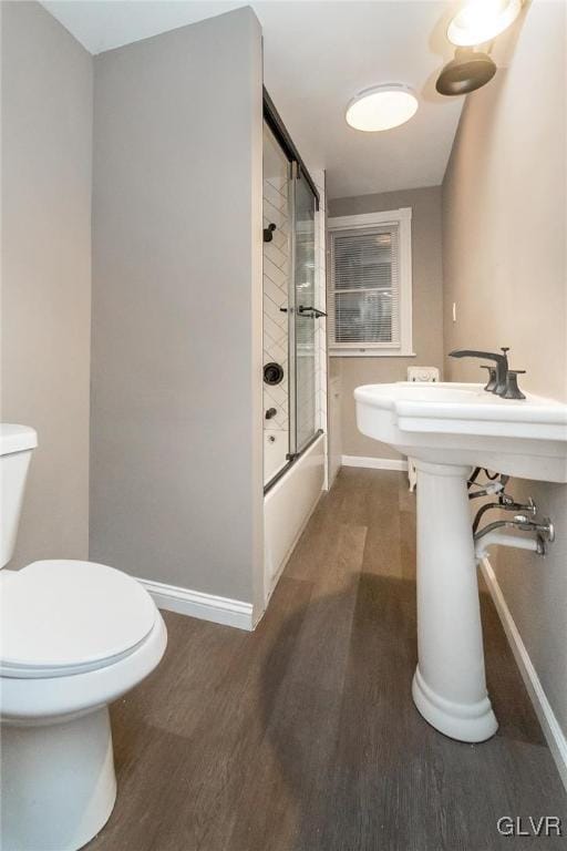 bathroom with bath / shower combo with glass door, hardwood / wood-style floors, and toilet