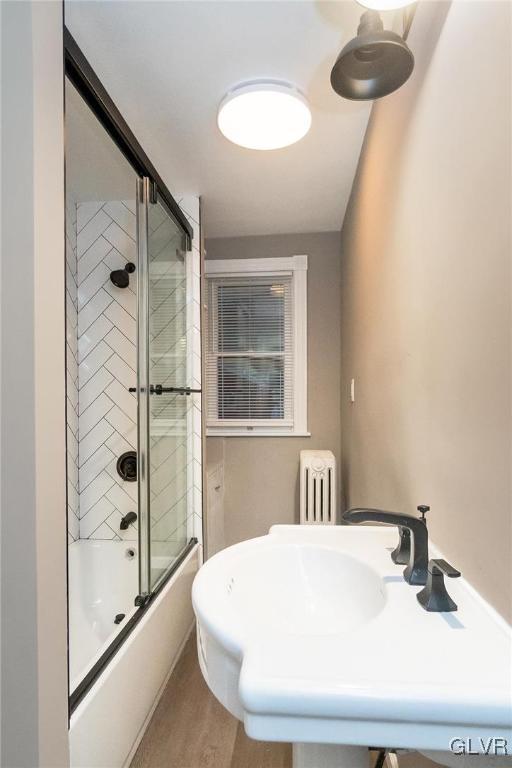 bathroom with combined bath / shower with glass door, sink, and radiator