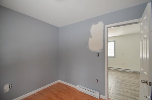 unfurnished room featuring a baseboard heating unit and light hardwood / wood-style floors