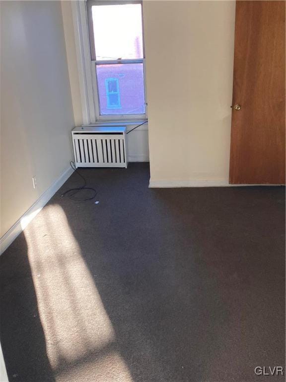 spare room featuring dark colored carpet and radiator heating unit