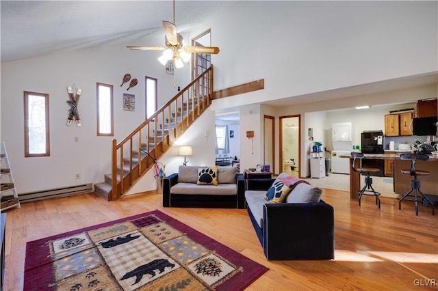 living room with ceiling fan, high vaulted ceiling, light wood-type flooring, and a baseboard heating unit