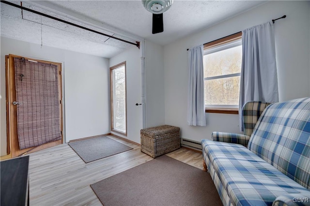 interior space with a baseboard heating unit, a textured ceiling, and light wood-type flooring