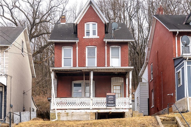 view of front of home with a chimney, a porch, and brick siding