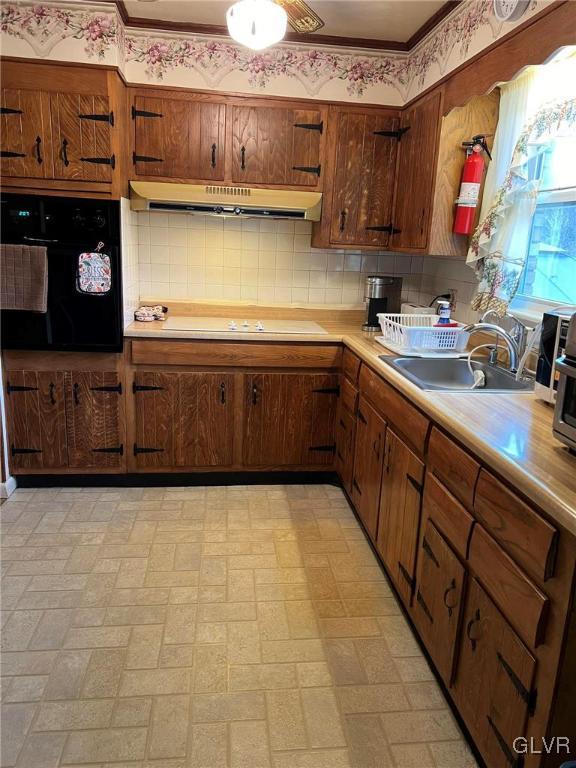 kitchen featuring sink, stovetop, tasteful backsplash, oven, and crown molding