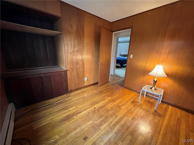 empty room with light hardwood / wood-style flooring, wood walls, and a baseboard heating unit