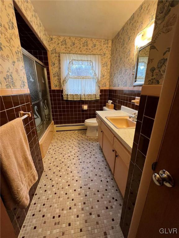 bathroom featuring tile walls, a baseboard heating unit, toilet, and a shower with shower door