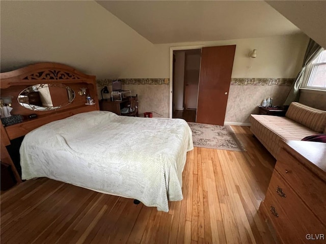 bedroom with light hardwood / wood-style floors, vaulted ceiling, and tile walls