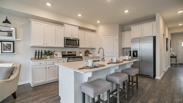 kitchen featuring white cabinetry, a kitchen island with sink, stainless steel appliances, and a kitchen bar