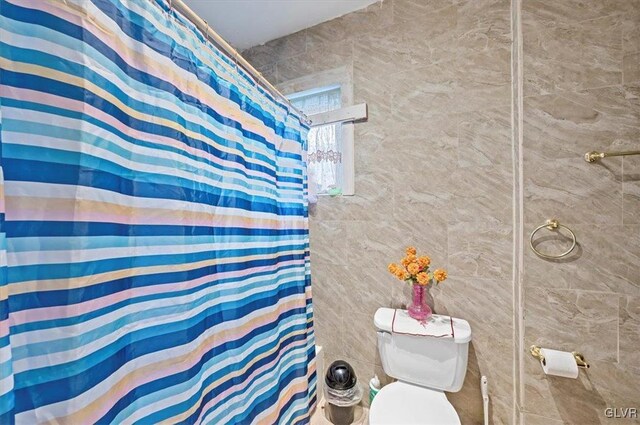 bathroom with a shower with curtain, toilet, and tile walls