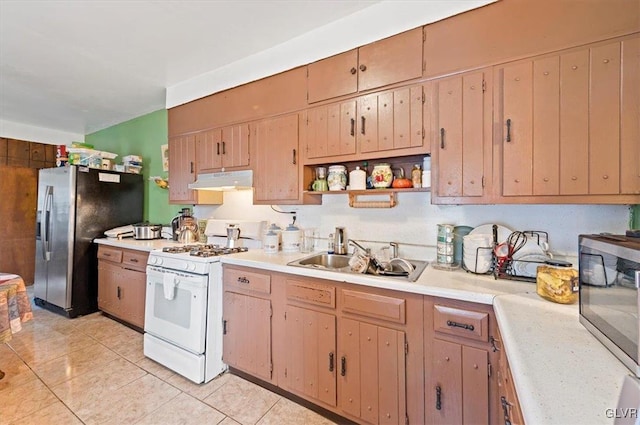 kitchen featuring white gas range, light tile patterned floors, stainless steel fridge, and sink