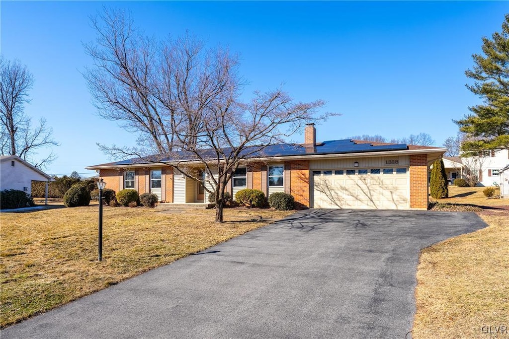 ranch-style home with a garage, a front lawn, and solar panels