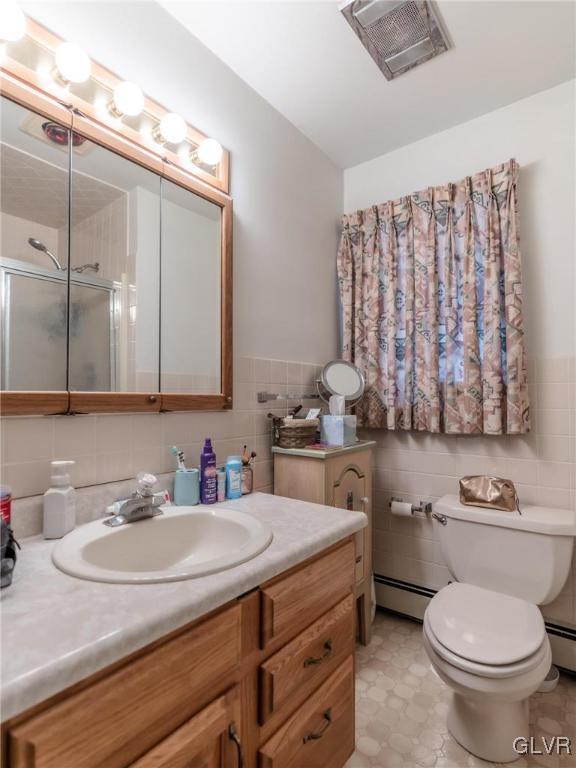 bathroom with toilet, a shower with shower door, tile walls, a baseboard radiator, and vanity