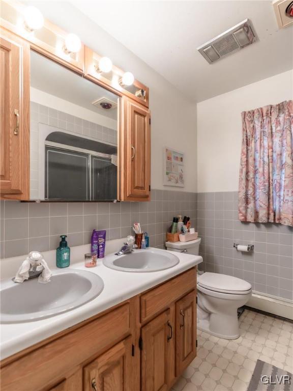 bathroom featuring tile walls, vanity, toilet, and walk in shower