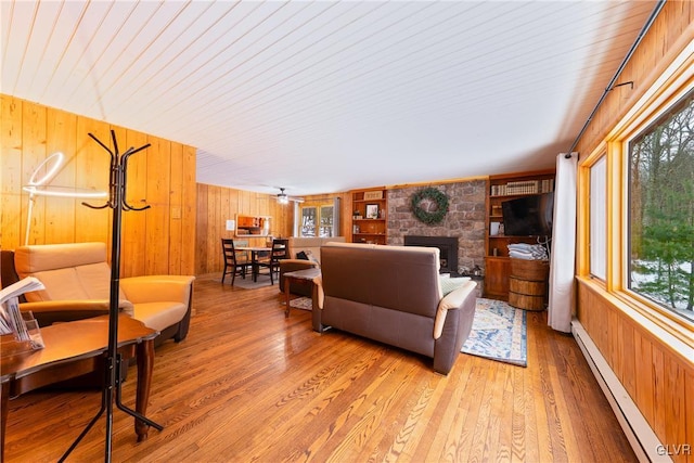 living room with a stone fireplace, a baseboard radiator, wood walls, and light wood-type flooring