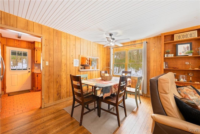 dining area with wood walls, ceiling fan, and light hardwood / wood-style flooring