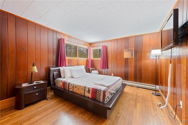 bedroom with a baseboard radiator, wood walls, and light hardwood / wood-style flooring