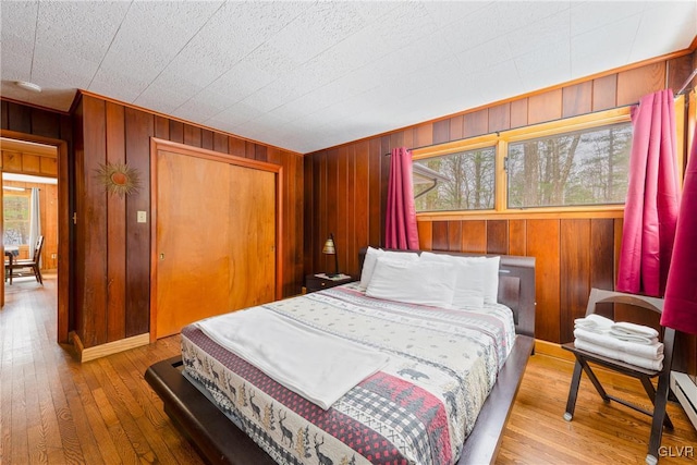 bedroom with a baseboard heating unit, hardwood / wood-style floors, wood walls, and a closet