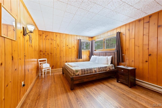 bedroom with hardwood / wood-style flooring, a baseboard radiator, and wooden walls