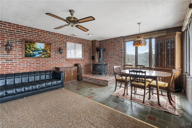 living room featuring ceiling fan, brick wall, a textured ceiling, and a wood stove