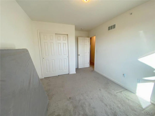 unfurnished bedroom with light colored carpet and a closet