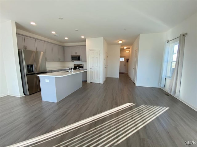 kitchen with stainless steel appliances, dark hardwood / wood-style flooring, gray cabinets, and a kitchen island with sink