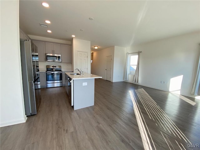 kitchen with sink, gray cabinetry, dark hardwood / wood-style floors, stainless steel appliances, and a kitchen island with sink