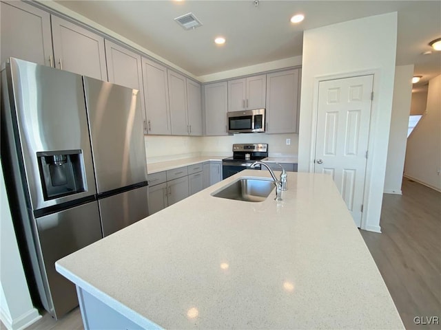 kitchen featuring light stone counters, sink, a center island with sink, and appliances with stainless steel finishes