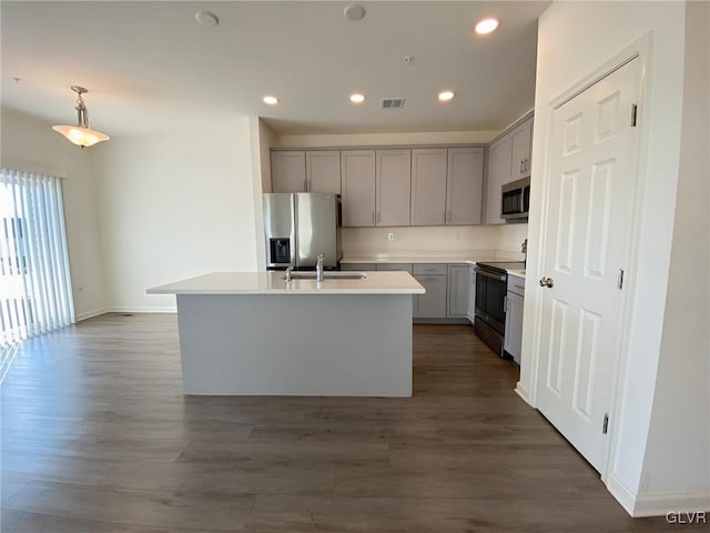 kitchen with dark wood-type flooring, sink, hanging light fixtures, appliances with stainless steel finishes, and a kitchen island with sink