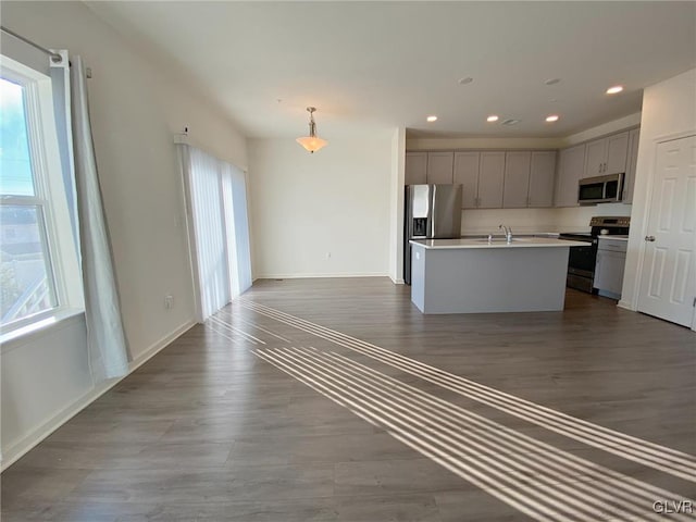 kitchen featuring decorative light fixtures, plenty of natural light, stainless steel appliances, and an island with sink