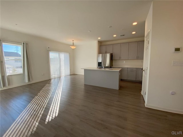 kitchen with a kitchen island with sink, pendant lighting, stainless steel fridge, and dark hardwood / wood-style floors