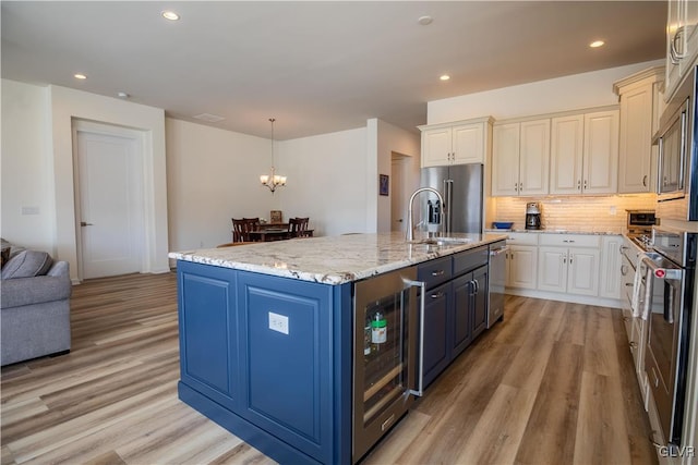 kitchen with decorative light fixtures, light hardwood / wood-style flooring, beverage cooler, light stone countertops, and a kitchen island with sink