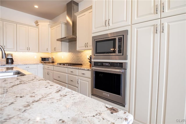 kitchen featuring sink, appliances with stainless steel finishes, backsplash, light stone countertops, and wall chimney exhaust hood