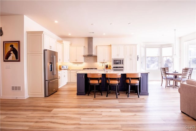 kitchen with stainless steel appliances, a kitchen bar, visible vents, backsplash, and wall chimney exhaust hood