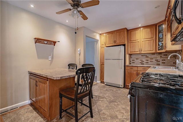 kitchen with decorative backsplash, black gas range, white refrigerator, sink, and a kitchen bar