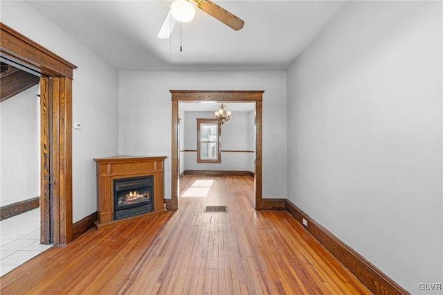 unfurnished living room featuring ceiling fan with notable chandelier and light hardwood / wood-style flooring