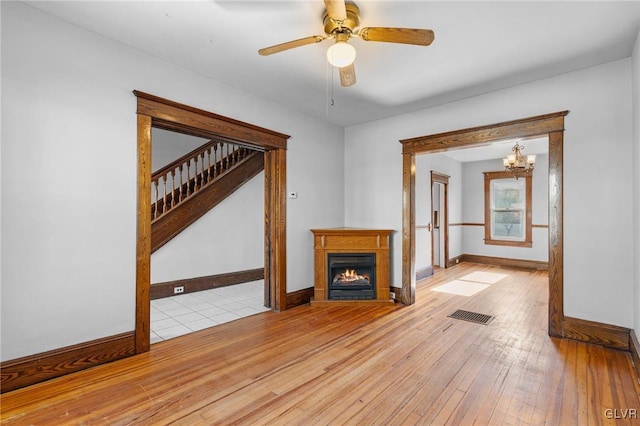 unfurnished living room featuring ceiling fan with notable chandelier and light hardwood / wood-style flooring