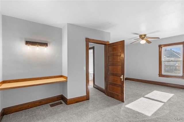 carpeted empty room featuring built in desk and ceiling fan