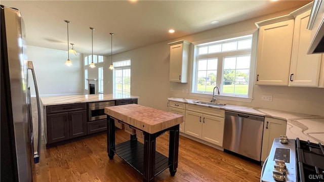 kitchen with appliances with stainless steel finishes, sink, white cabinetry, pendant lighting, and dark hardwood / wood-style flooring