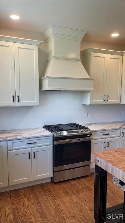 kitchen with wood-type flooring, custom exhaust hood, wooden counters, stainless steel gas stove, and white cabinets