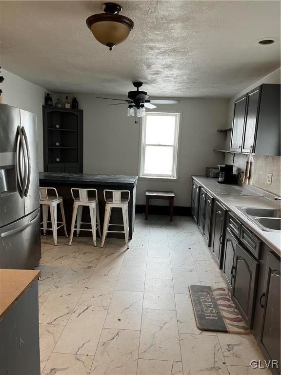 kitchen with ceiling fan, sink, a textured ceiling, and stainless steel fridge